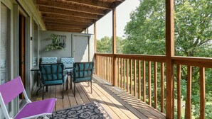 A wooden deck with a table and chairs, a covered area with a railing, and a view of trees. - Welcome Inn- Pools - Great Balcony - Trails to Fishing -SO Close to Sdc!! (Branson West)