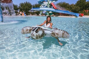 A pool area with a water slide and a person in a turtle float.