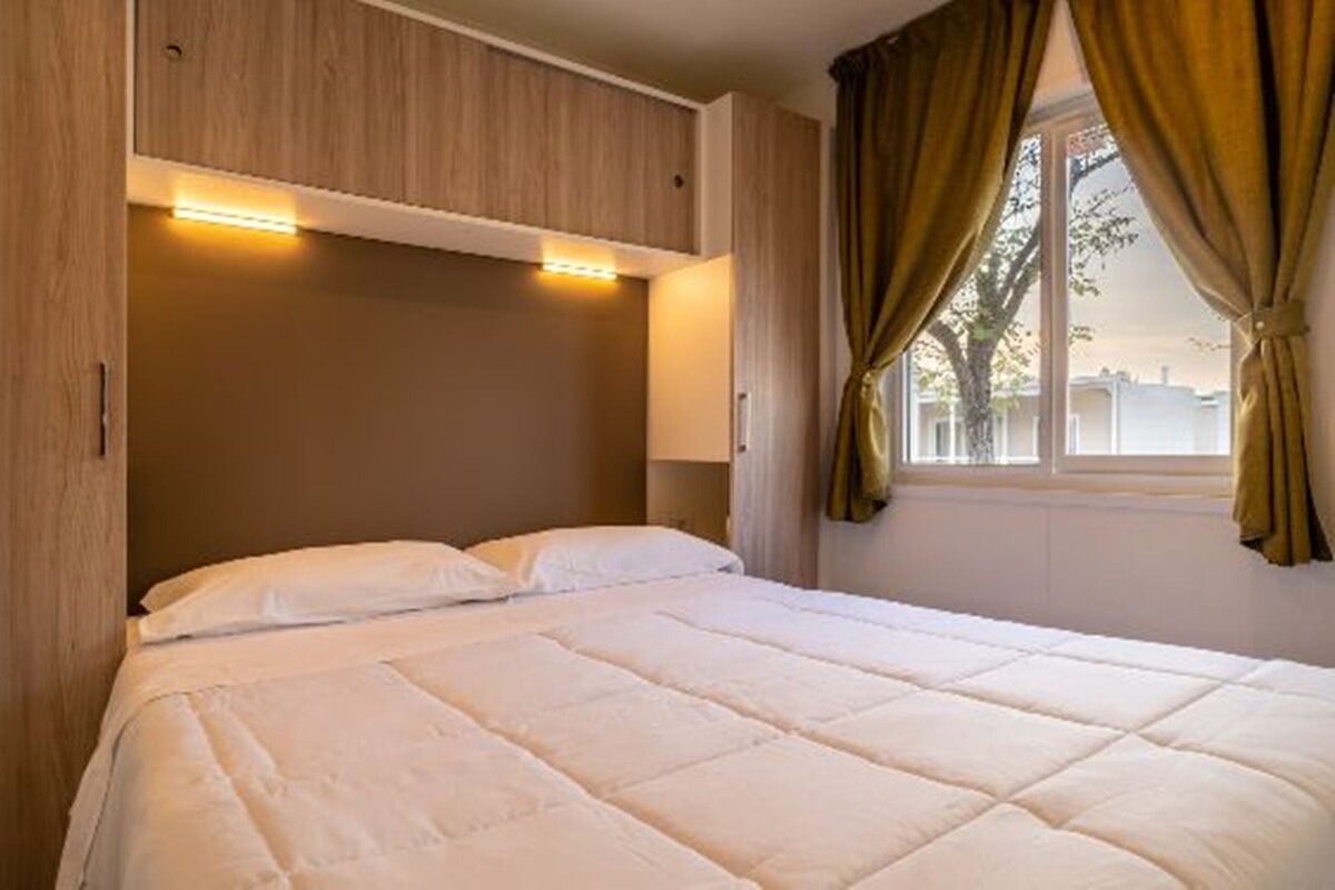 A hotel room with a bed, wooden headboard, and a window with curtains.