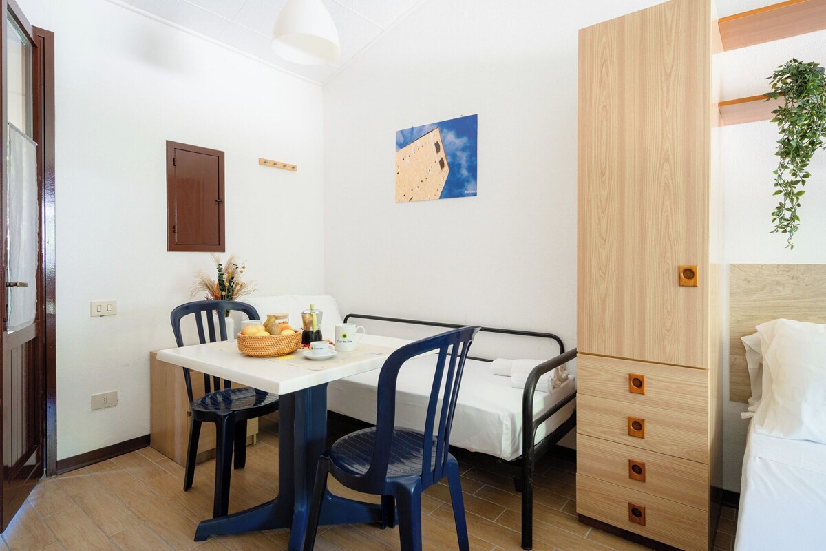 A small, clean room with a bed, a table with chairs, a wooden cabinet, and a wall-mounted picture.