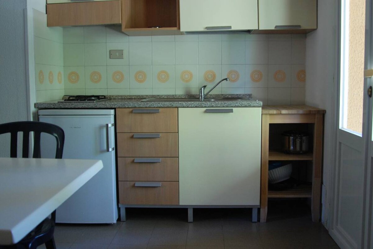 A compact kitchen with a refrigerator, stove, sink, and wooden cabinets.