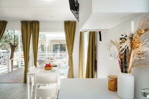 A dining area with a white table, chairs, a bowl of fruit, and a vase with dried plants. - Club del Sole La Risacca Family Collection (Porto Sant'Elpidio)
