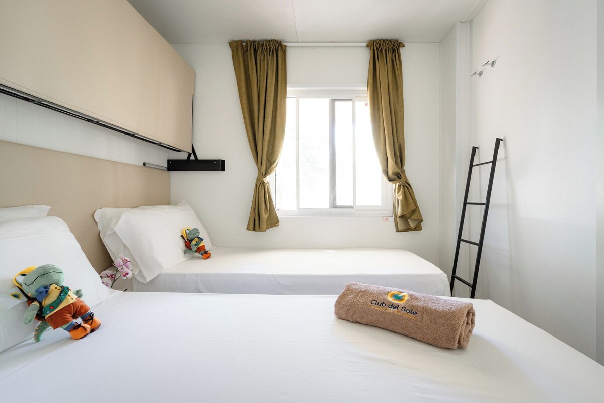 A hotel room with two beds, a window with curtains, a towel with a logo, and a ladder against the wall.