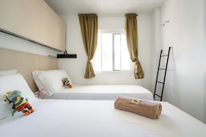 A hotel room with two beds, a window with curtains, a towel with a logo, and a ladder against the wall. - Club del Sole La Risacca Family Collection (Porto Sant'Elpidio)