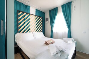 Ett hotellrum med en säng, turkosa gardiner, en randig sänggavel och prydligt hopvikta handdukar.