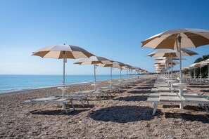 A beach with rows of white lounge chairs and beige umbrellas.