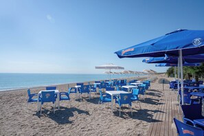 A beachside restaurant with blue chairs and umbrellas, a wooden deck, and a view of the sea.