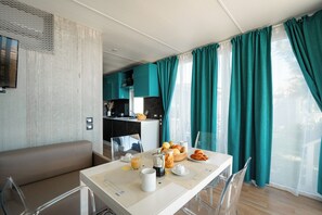 A modern room with a dining table set with breakfast items, a sofa, and a kitchen area in the background.