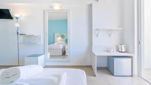 A modern hotel room with a bed, a desk, a small refrigerator, and a mirror reflecting a bathroom with a blue wall and a white sink. - Santa Maria City Hotel (Rhodes)