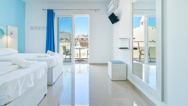 A hotel room with two beds, a balcony with a table and chairs, and a large window. - Santa Maria City Hotel (Rhodes)