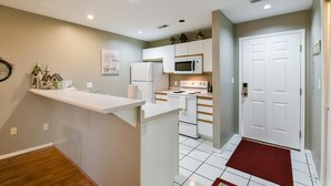 Una cocina compacta con armarios blancos, un microondas, un refrigerador y una estufa.