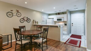 Cocina compacta con armarios blancos, un microondas y un refrigerador. Hay un comedor con una mesa y sillas de madera, y dos bicicletas colgadas en la pared.