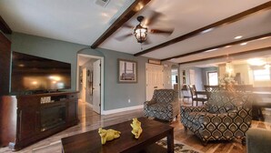 A living room with a dark wooden coffee table, patterned armchairs, a television, and a ceiling fan. - Solace Space at Foothills - Close To All Of Branson - Luxury Comfort (Branson)