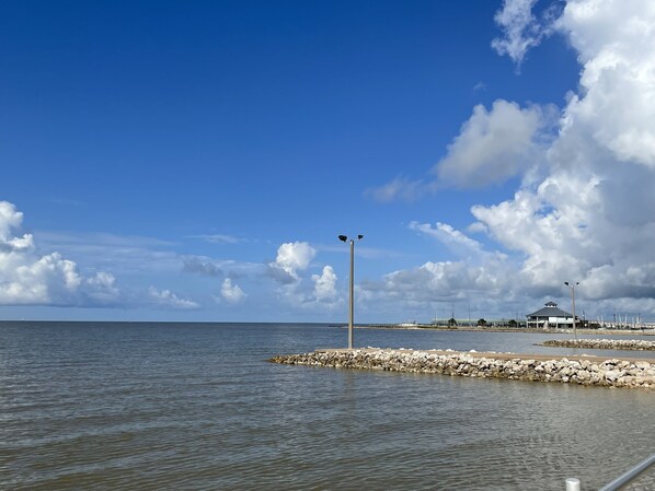A coastal view with a clear sky, calm sea, and a rocky breakwater. - Bay View Cottage - 1 block to lighted fishing piers, parks, boat ramp & more. (Palacios)