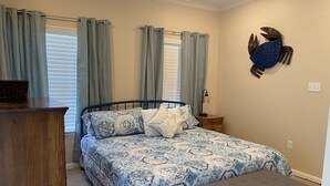 Un dormitorio con una cama, un aparador de madera, un reposapiés gris y un adorno de cangrejo en la pared.