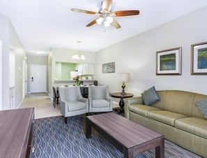 A living room with a sofa, two armchairs, a coffee table, a dining area with a table and chairs, a kitchen in the background, and a ceiling fan. - NEAR DISNEY! 1 BR Condo - SLEEPS 4, Tennis, Baby Pool, Tennis, Shuffleboard, etc (Kissimmee)