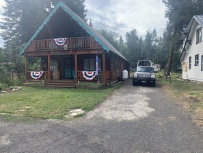 Une cabane avec une véranda, un camion garé devant et une maison sur la droite.