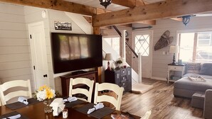 Uma área de refeições com uma mesa de madeira posta para quatro pessoas, uma televisão acima da mesa e uma escada que leva a outro andar.