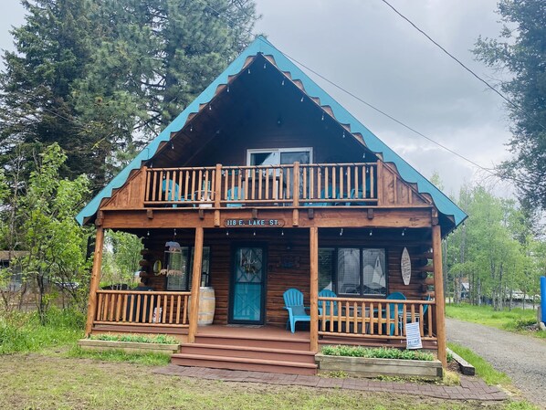 A cabin with a balcony, a porch with chairs, and a sign reading "118 E. LAKE ST."