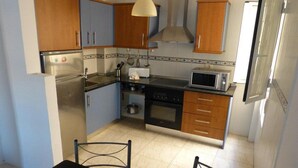 A compact kitchen with wooden cabinets, a stainless steel refrigerator, a microwave, and a stove. - Suncanarias Apartamento Marina (San Miguel de Abona)
