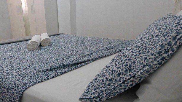 A neatly made bed with a patterned bedspread and pillows, two rolled towels on the bed, and a window with blinds in the background. - Suncanarias Apartamento Marina (San Miguel de Abona)