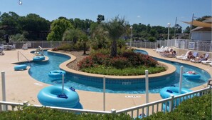 Una piscina con múltiples carriles, rodeada de un área ajardinada con palmeras y flores rojas.