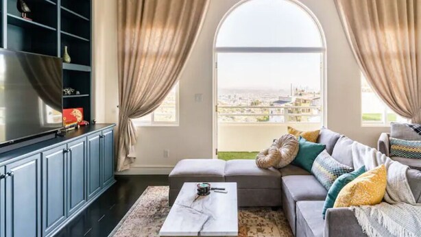 Una sala de estar moderna con un ventanal grande, un sofá gris, una mesa de centro y un televisor sobre un mueble.