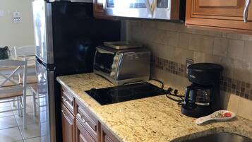 A kitchen with wooden cabinets, a stainless steel refrigerator, a microwave, a toaster, a coffee maker, and a granite countertop.