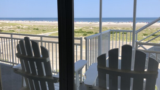 A balcony with white chairs and a view of the beach.