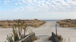 A sandy beach path leading to the ocean, with dunes on either side and a wooden boardwalk.