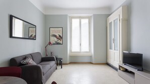 A living room with a sofa, a TV, a window, and a framed picture on the wall. - Hostmate - Milano - Cantoni - Washington  (Milano)