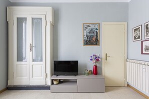 A room with a television on a stand, a door, and a wall with framed pictures.