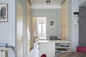 A hotel room with a kitchenette, a dining area, a bed, and a view of the street.
