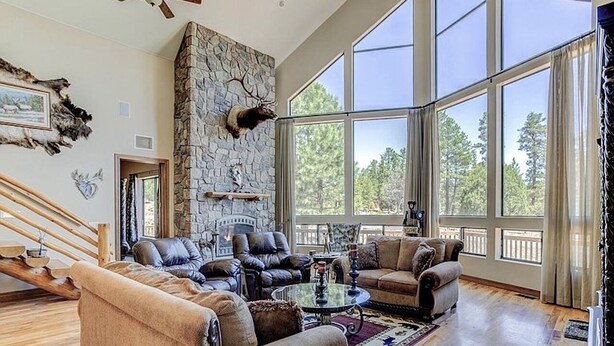 A spacious living room with a stone fireplace, leather sofas, and large windows offering a view of the outdoors. - The EXECUTIVE LEVEL retreat for families and outdoor lovers in Happy Jack, AZ! (Happy Jack)