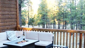A wooden deck with a wicker sofa and a table with a bottle and glass. - The EXECUTIVE LEVEL retreat for families and outdoor lovers in Happy Jack, AZ! (Happy Jack)