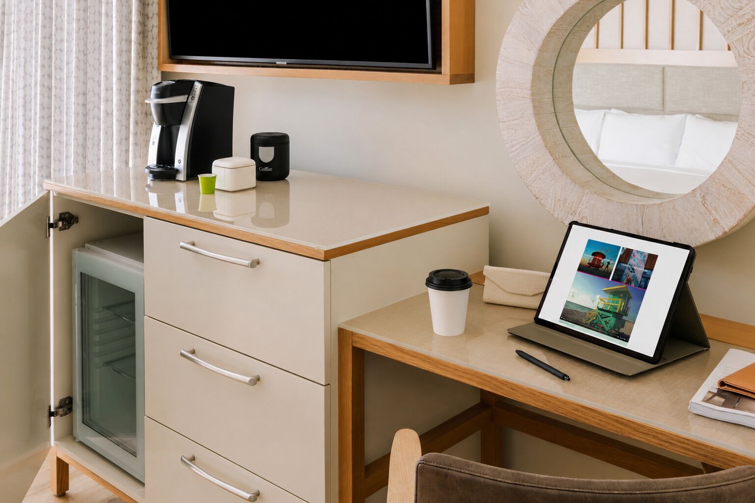 Una habitación de hotel con escritorio, cafetera, ordenador portátil, taza y televisor.