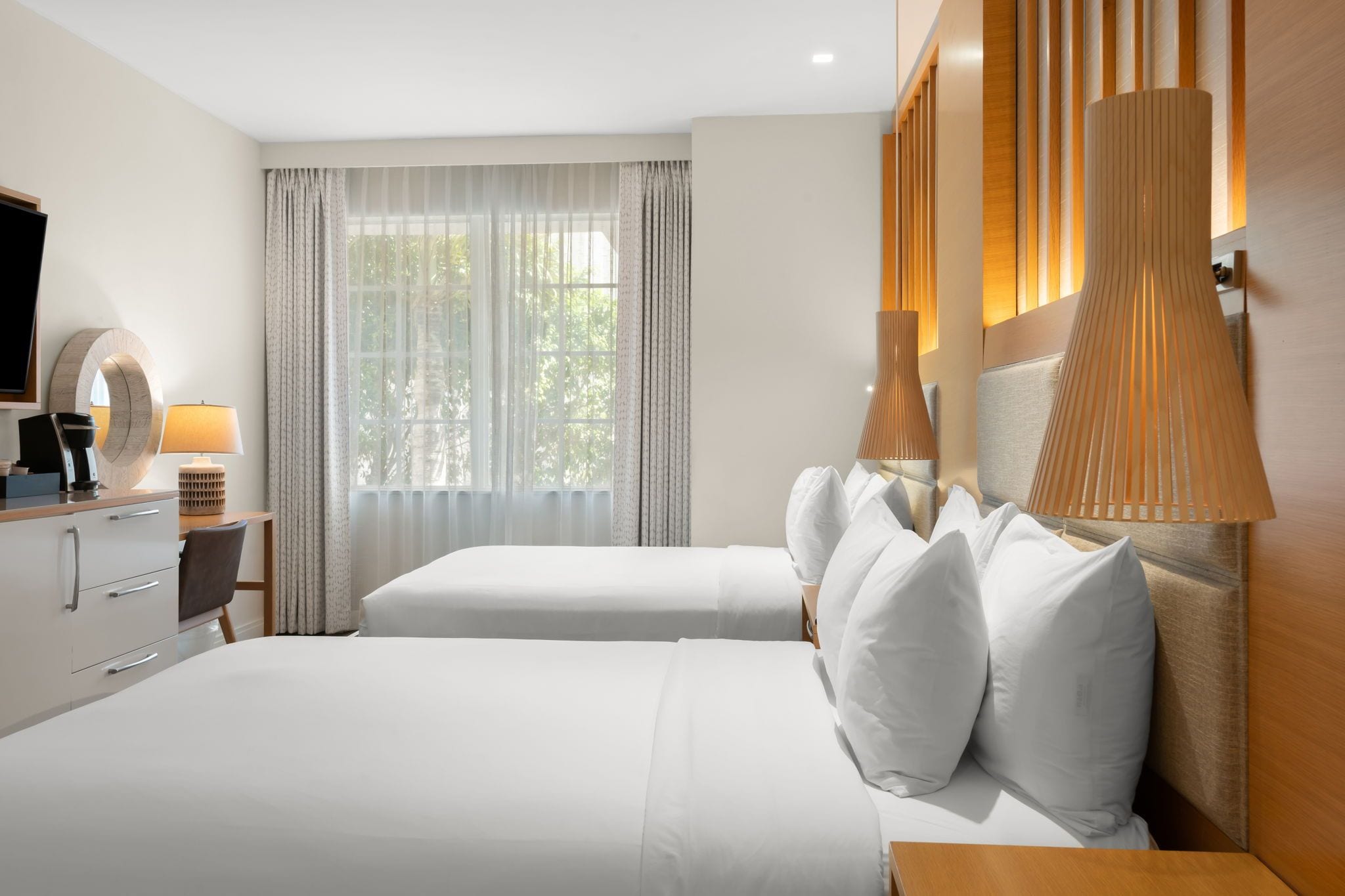 A hotel room with a bed, bedside tables, a lamp, a TV, and a window with curtains.