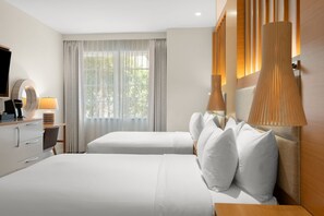 Une chambre d’hôtel avec un lit, des tables de chevet, une lampe, une télévision et une fenêtre avec des rideaux.