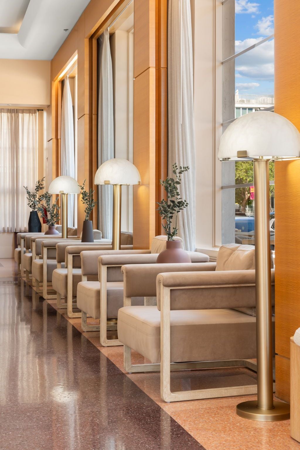 A hotel lobby with rows of seating, large windows, and floor lamps.