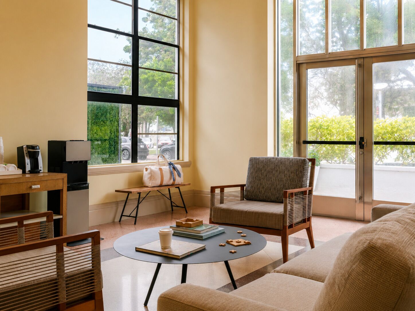 Una habitación con cafetera, una mesa con una taza y libros, una silla y un ventanal con vistas al exterior.