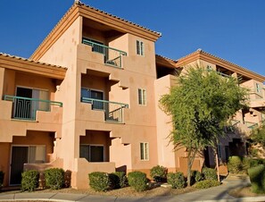 A multi-story building with balconies, a clear sky, and a well-maintained garden.
