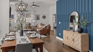 Ein modernes Wohnzimmer mit Essbereich, ausgestattet mit einem Holztisch, der mit weißen Tellern und Schüsseln gedeckt ist, einer braunen Ledersofa und einer blauen Akzentwand.