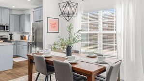 Eine moderne Küche mit grauen Schränken, Edelstahlgeräten und einem Essbereich mit einem Holztisch und grauen Stühlen.