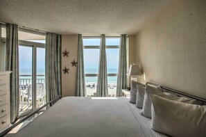 A hotel room with a large bed, a view of the beach, and a balcony with chairs. - Bay Watch Condo w/ Oceanfront Balcony & Beach View (North Myrtle Beach)