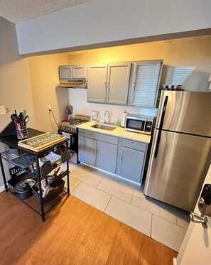 A compact kitchen with a gas stove, microwave, stainless steel refrigerator, and grey cabinets.