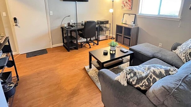 Ein Wohnzimmer mit grauem Sofa, einem Couchtisch, einem Fernseher und einem Schreibtisch mit Stuhl.