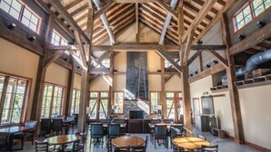 Een ruime binnenruimte met hoge plafonds en zichtbare houten balken, met meerdere tafels en stoelen voor eten of gezellig samenzijn.