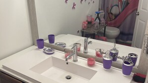 A bathroom with a white sink, purple cups, and a mirror reflecting a toilet and shower curtain. - GORGEOUS 1/1 CONDO (Lauderdale Lakes)