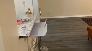 A modern kitchen with a marble countertop, two bar stools, a small Buddha statue, and a dark wooden floor. - GORGEOUS 1/1 CONDO (Lauderdale Lakes)