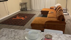 A living room with a brown sofa, a marble coffee table, and a white wall-mounted TV. - GORGEOUS 1/1 CONDO (Lauderdale Lakes)